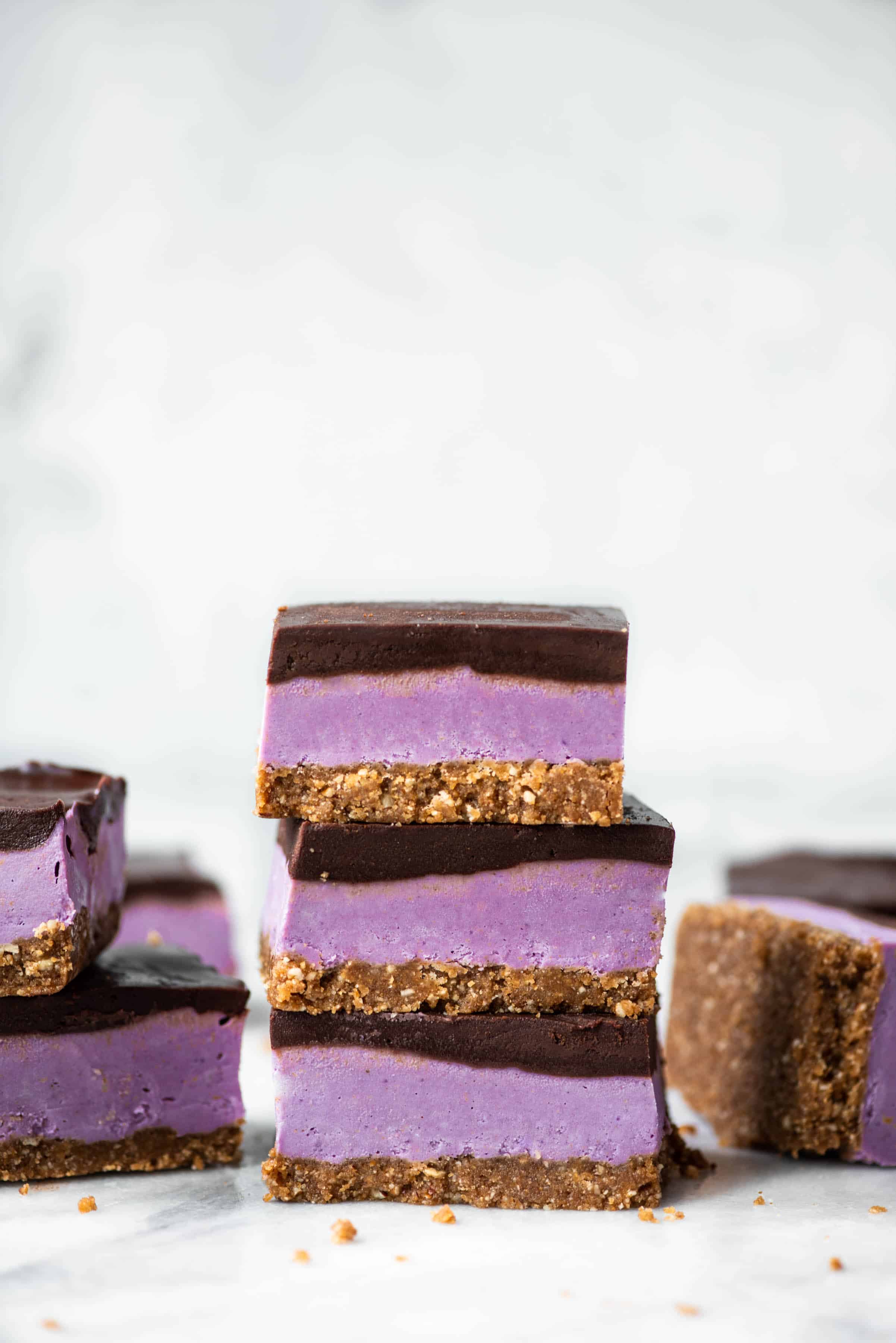Stack of purple sweet potato cheesecake bars with chocolate ganache on white background