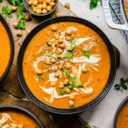 Overhead view of red lentil soup with a garnish of chickpeas, cream, and herbs.