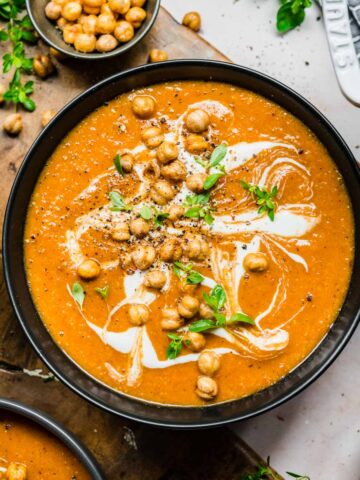 Overhead view of red lentil soup with a garnish of chickpeas, cream, and herbs.