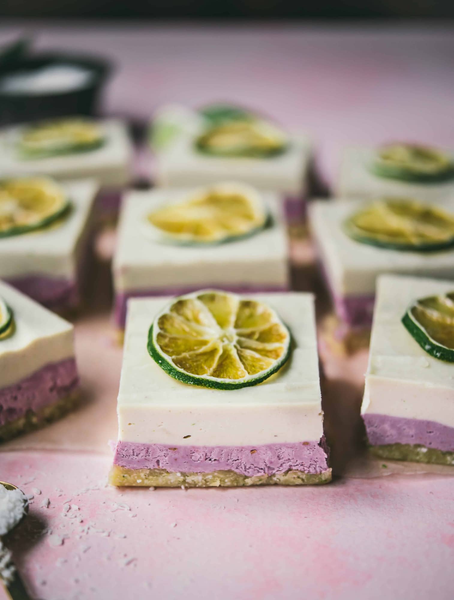 Side view of coconut lime raspberry cheesecake bars with lime slices on top