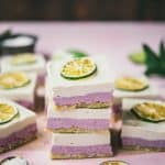 Three stacked coconut lime raspberry cheesecake bars on a pink background