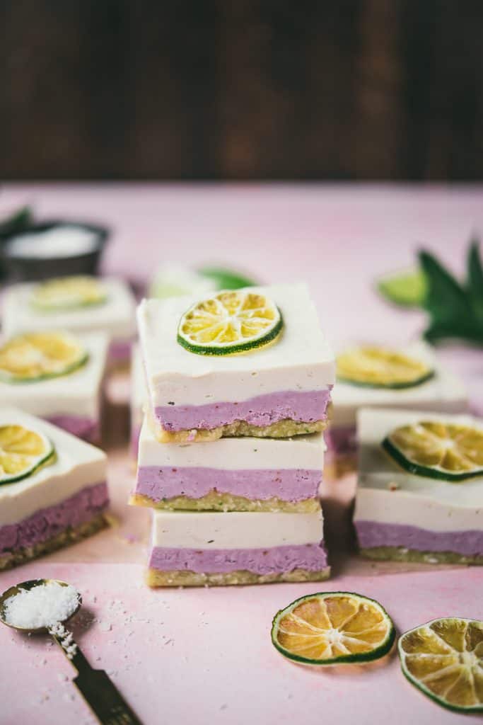 Three stacked coconut lime raspberry cheesecake bars on a pink background