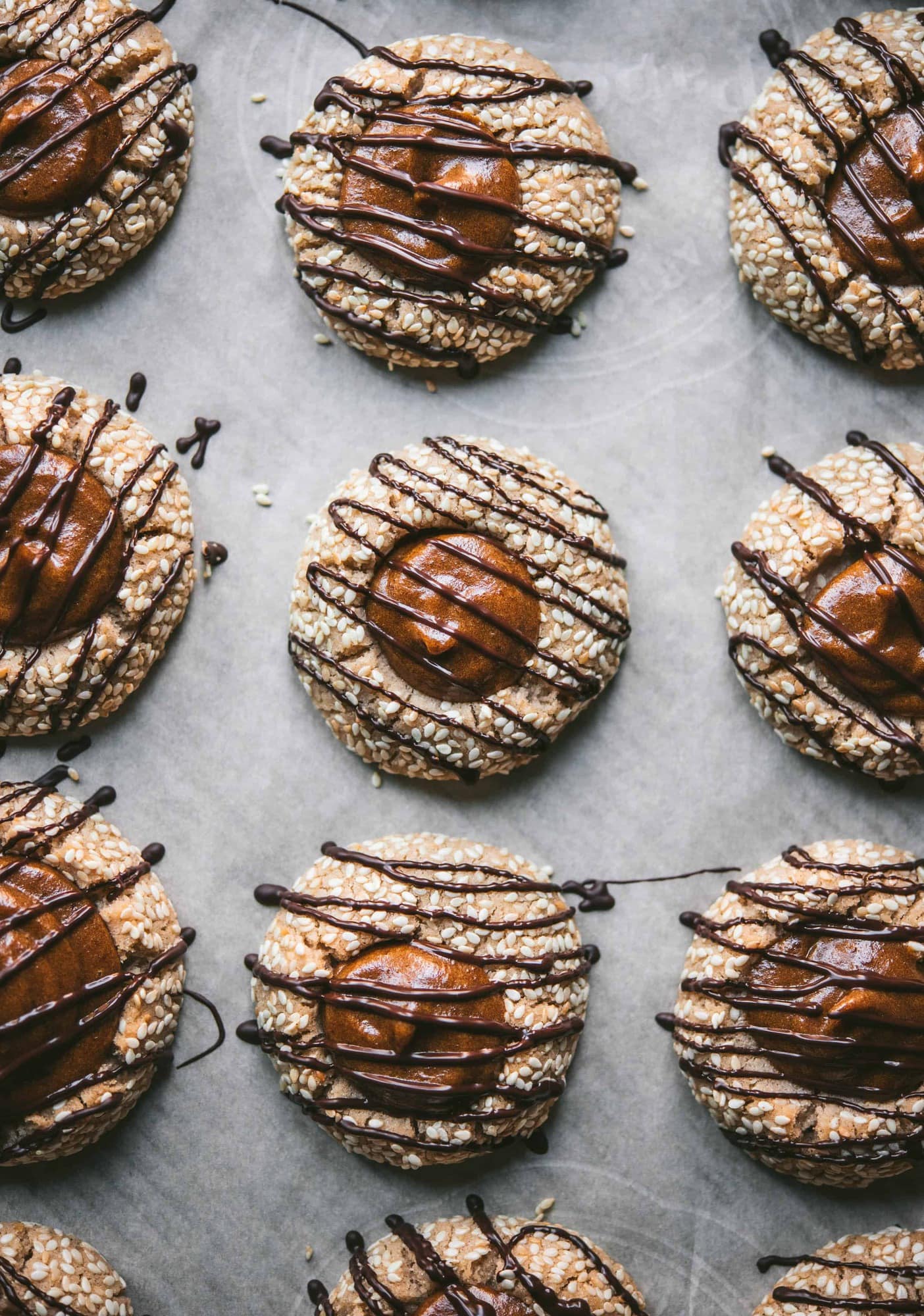 Overhead of tahini thumbprint cookies with date filling and chocolate drizzle on parchment paper