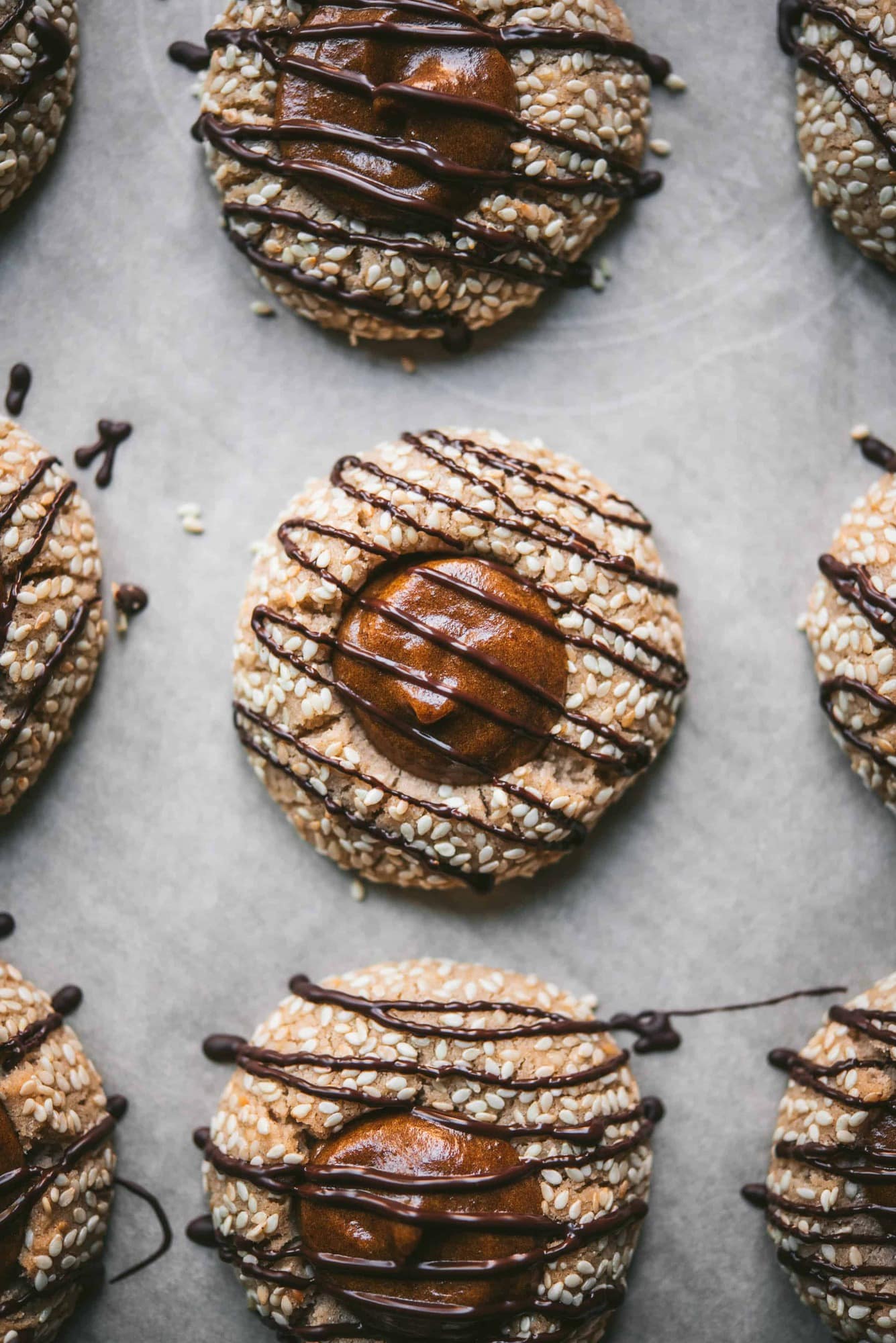 Close up of tahini thumbprint cookies with date filling and chocolate drizzle on parchment paper