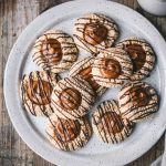 Overhead of tahini thumbprint cookies with date filling and chocolate drizzle on a white plate