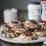 Side view of tahini thumbprint cookies with date filling and chocolate drizzle on a white plate