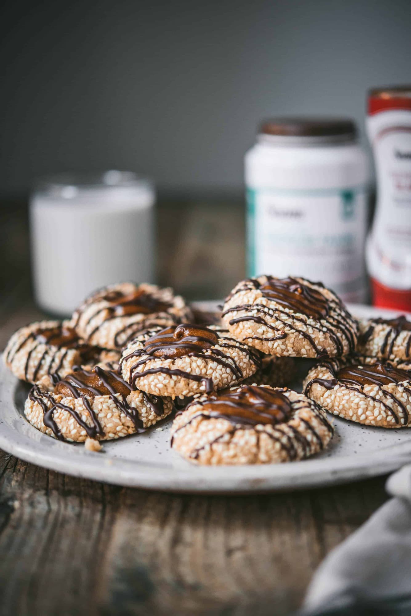 Side view of tahini thumbprint cookies with date filling and chocolate drizzle on a white plate