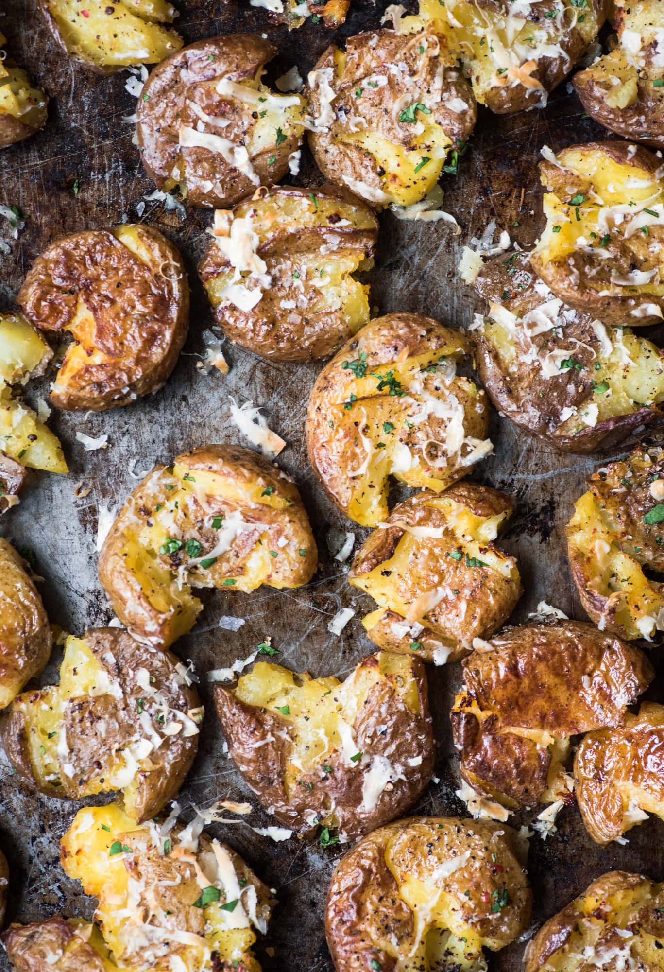 Close up overhead of crispy smashed potatoes with vegan parmesan and herbs