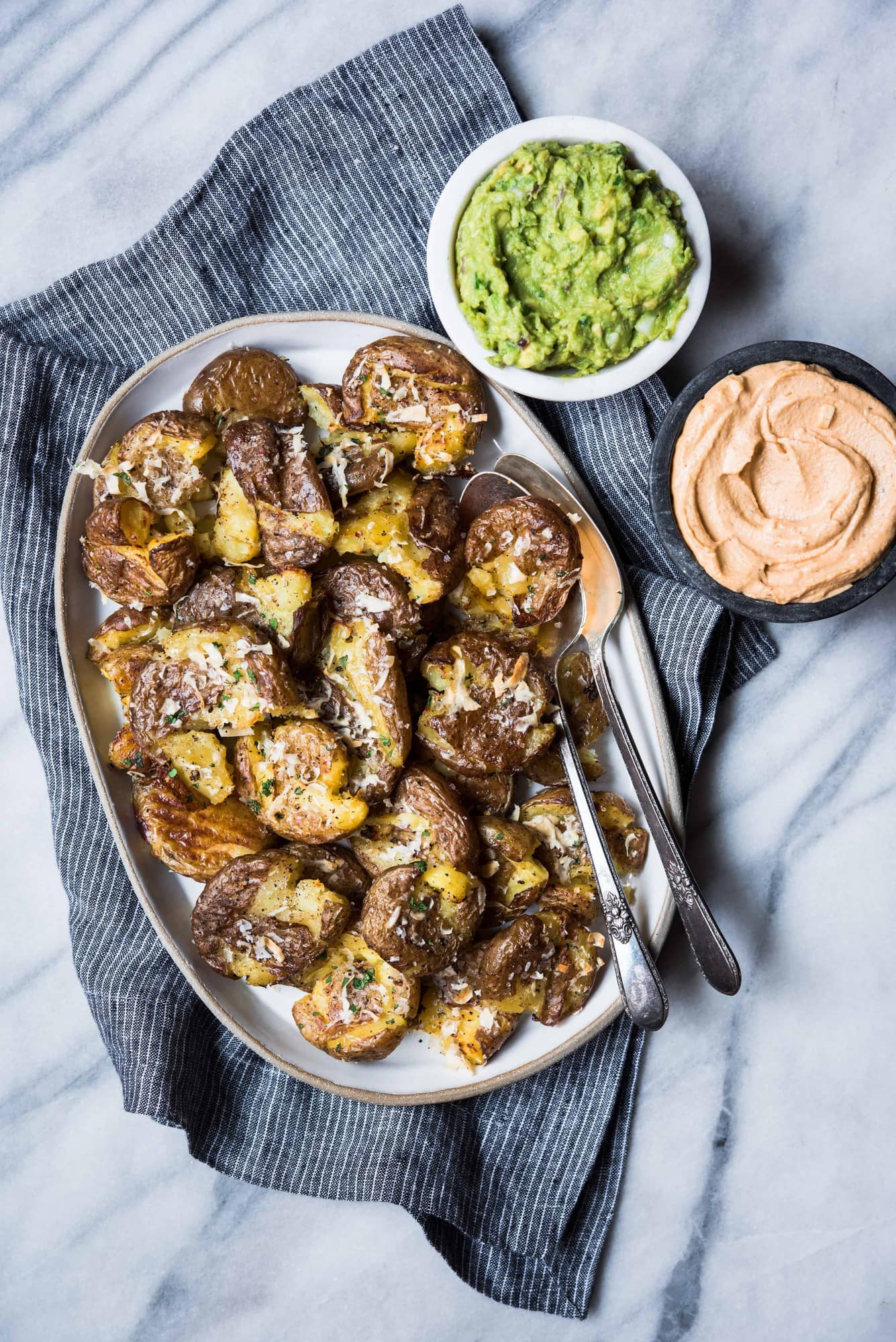 Platter of crispy smashed potatoes on marble background with guacamole and queso dip