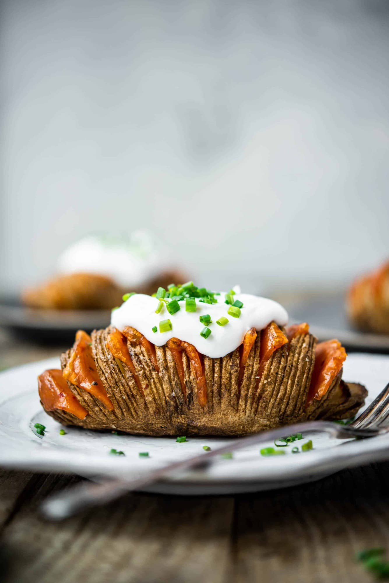 Side view of vegan cheesy hasselback potato on a white plate