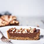Side view of slice of chocolate hazelnut ganache tart on a white plate with fork