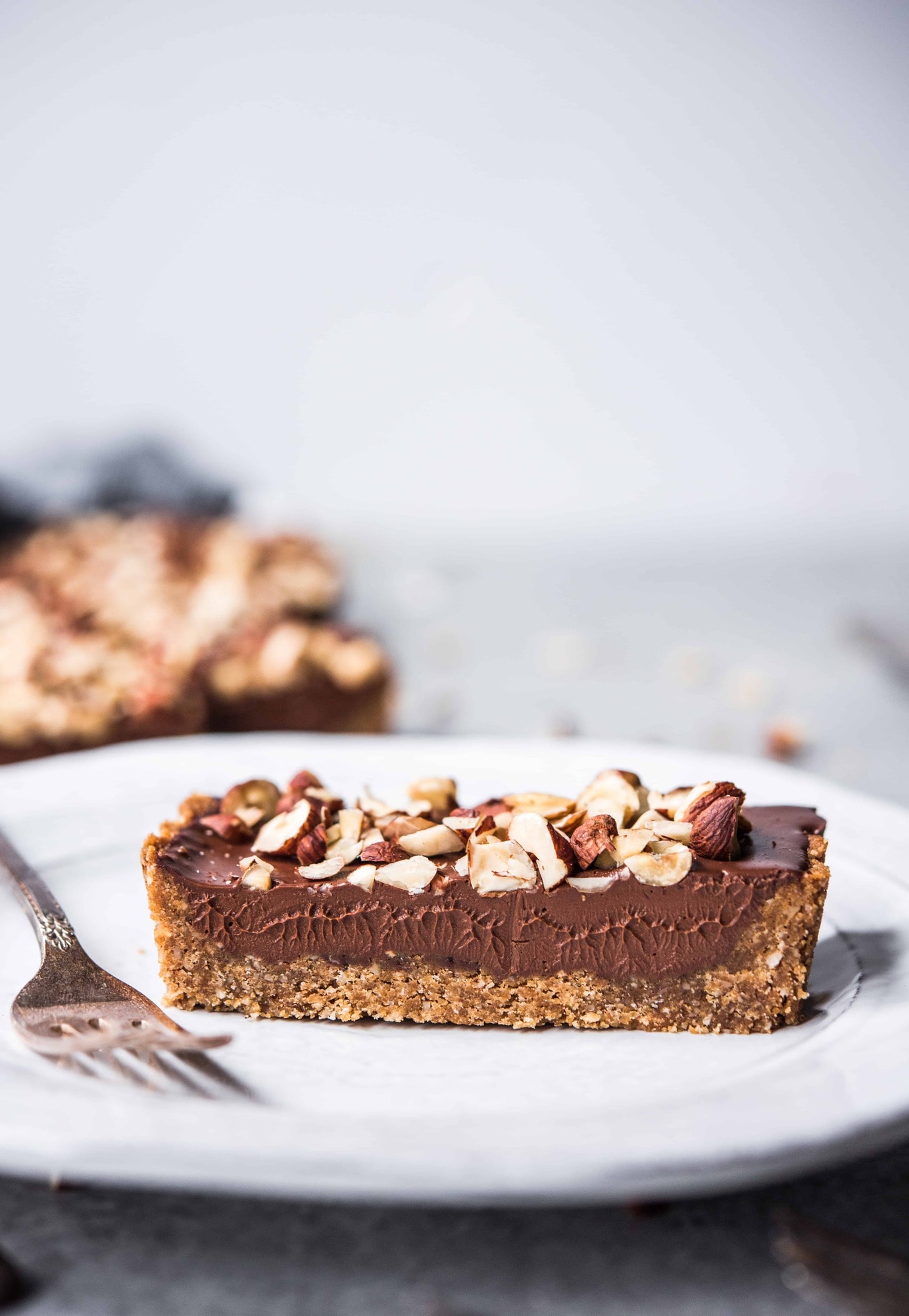 Side view of slice of chocolate hazelnut ganache tart on a white plate with fork