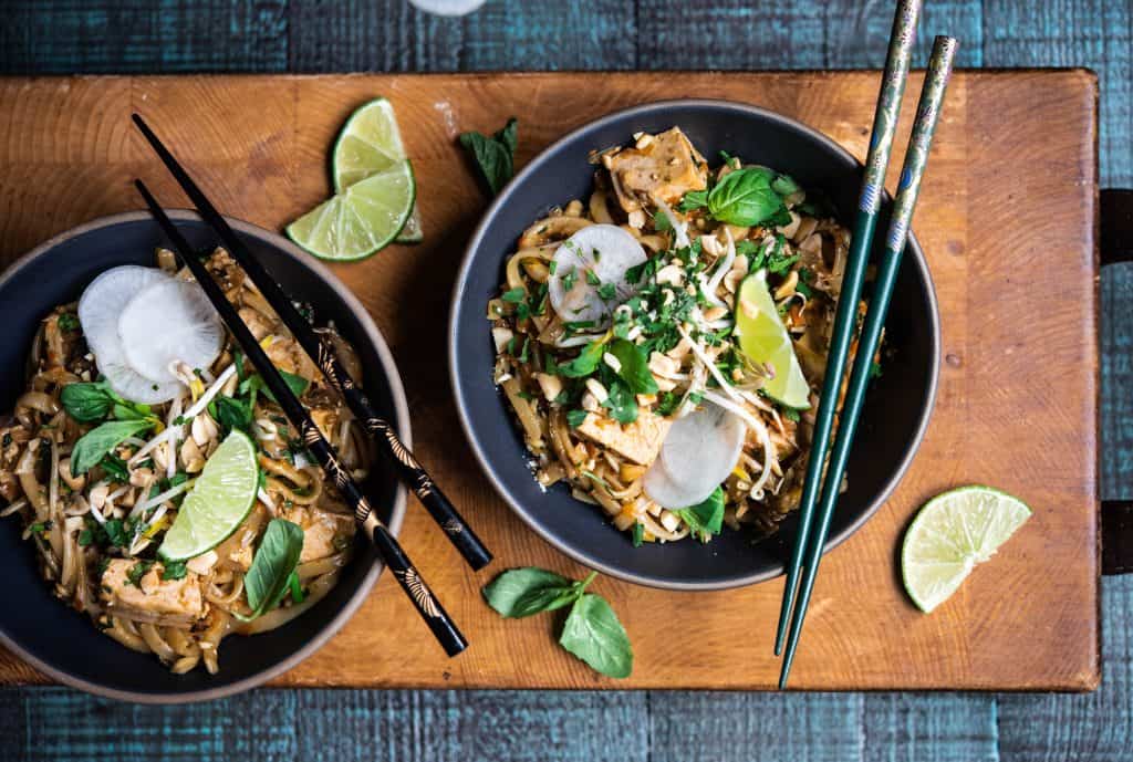 Two bowls of vegan pad thai with chopsticks on rustic wood background