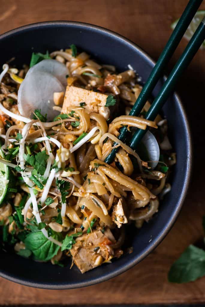 Close up of vegan pad thai noodles wrapped around chopsticks in a dark grey bowl