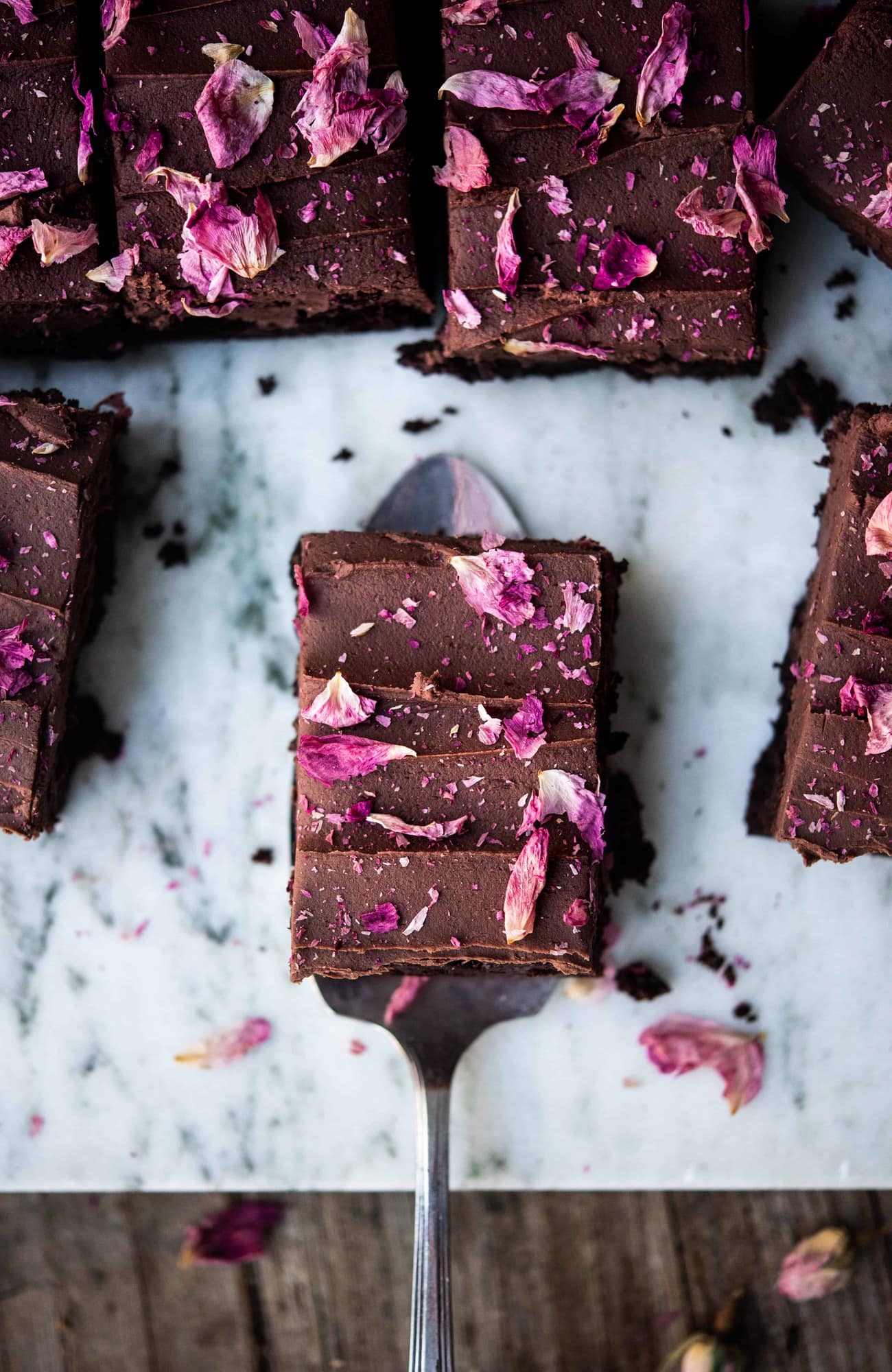 Overhead close up of one chocolate ganache brownie with rose petals on serving utensil