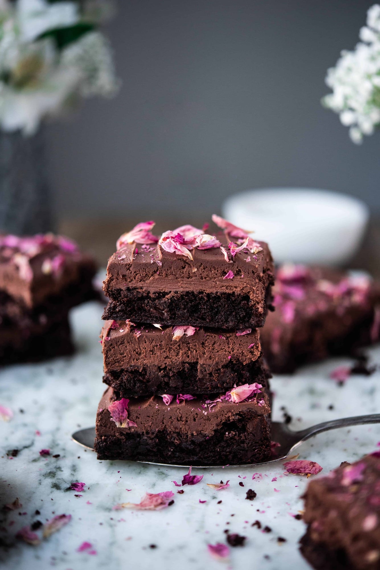 Side view of three stacked chocolate ganache brownies with rose petals on white marble