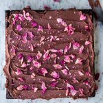 Overhead close up of chocolate ganache frosting brownies with rose petals