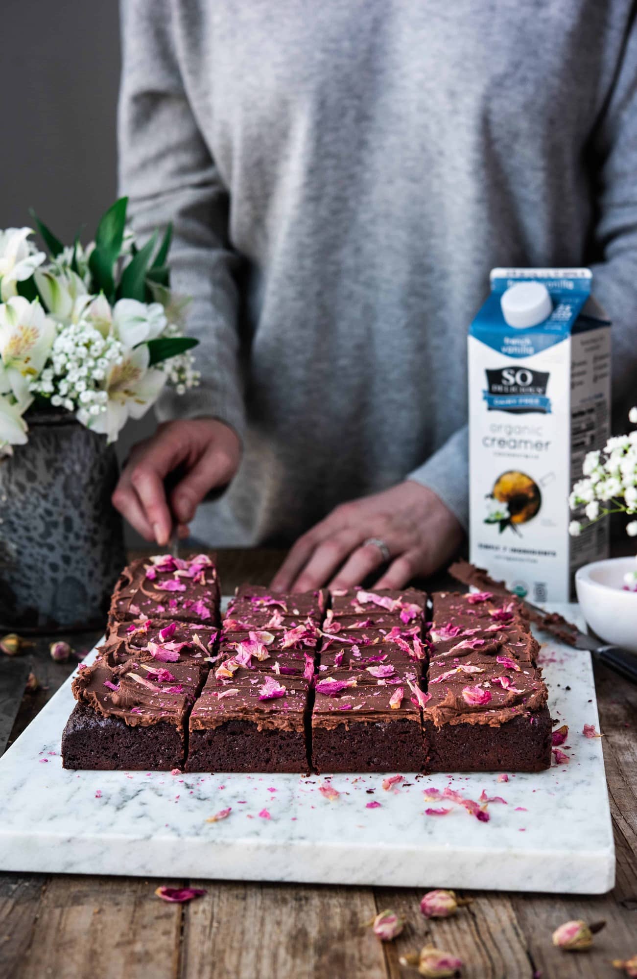 Side view of person cutting chocolate ganache brownies with rose petals