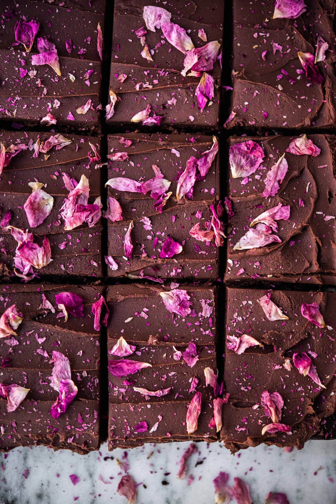 Overhead close up of chocolate ganache frosting brownies with rose petals