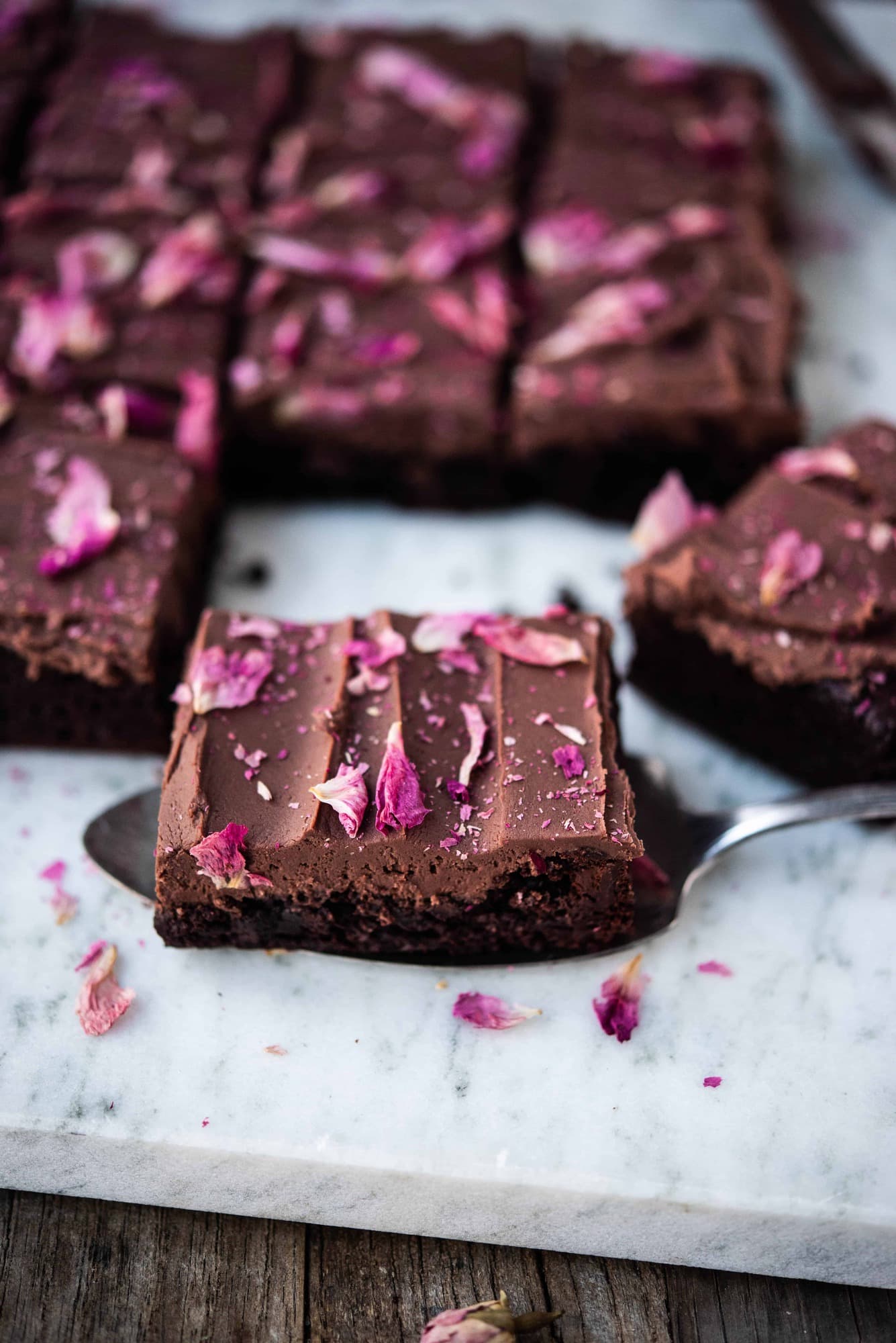 Side view of one chocolate ganache brownie with frosting and rose petals