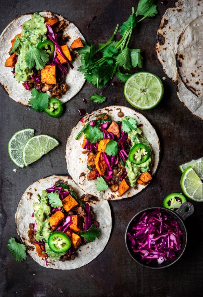 Overhead view of vegan lentil walnut tacos with roasted sweet potatoes, cabbage and guacamole on an antique serving tray