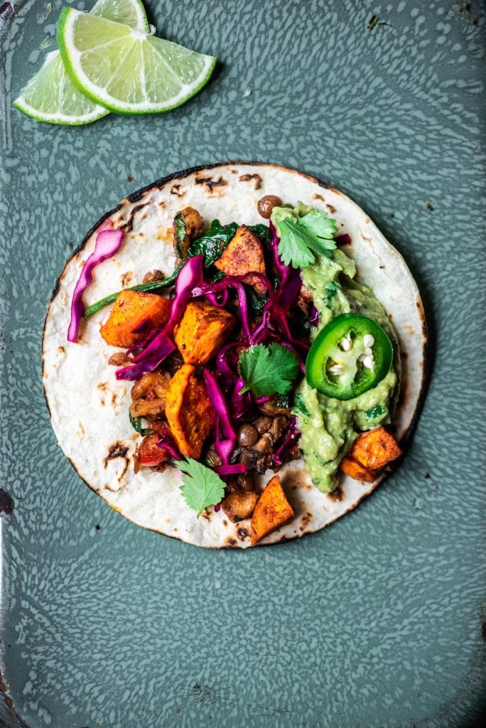 Overhead view of vegan lentil walnut tacos with roasted sweet potatoes, cabbage and guacamole on an antique serving tray