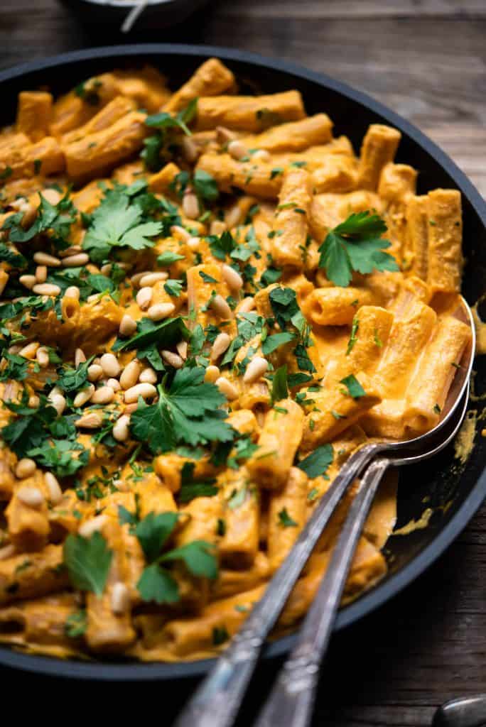 Close up of roasted red pepper vegan pasta in a saute pan on a wood table