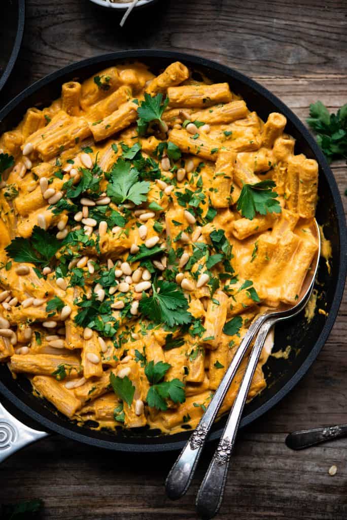 Overhead of roasted red pepper vegan pasta in a saute pan on a wood table