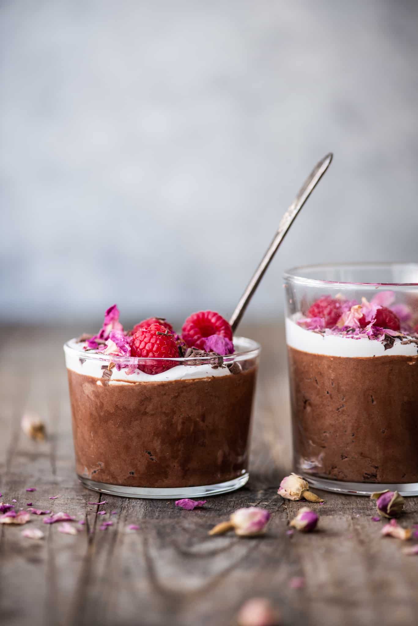 Side view of vegan chocolate mousse in a small jar with whipped cream, shaved chocolate and raspberries