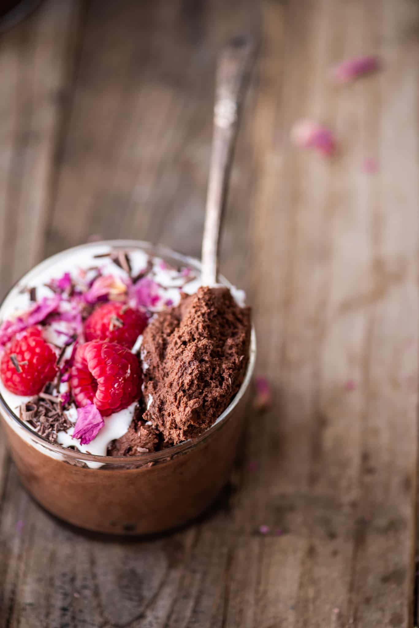 Overhead of vegan chocolate mousse in a small jar with whipped cream, shaved chocolate, rose petals and raspberries