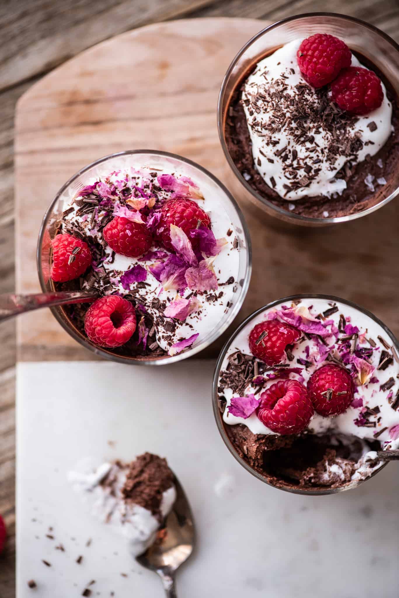 Overhead of vegan chocolate mousse in a small jar with whipped cream, shaved chocolate, rose petals and raspberries