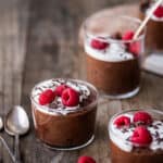 Side view of vegan chocolate mousse in a small jar with whipped cream, shaved chocolate and raspberries