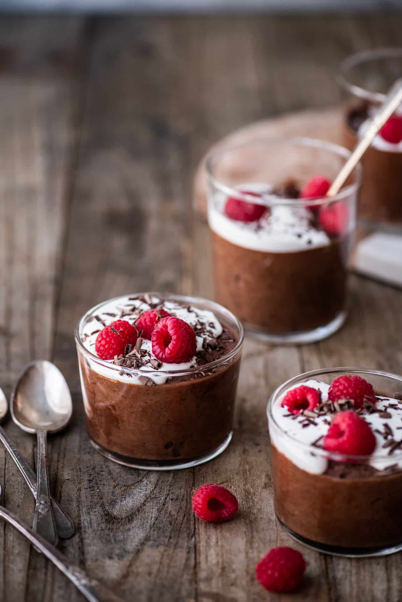 Side view of vegan chocolate mousse in a small jar with whipped cream, shaved chocolate and raspberries