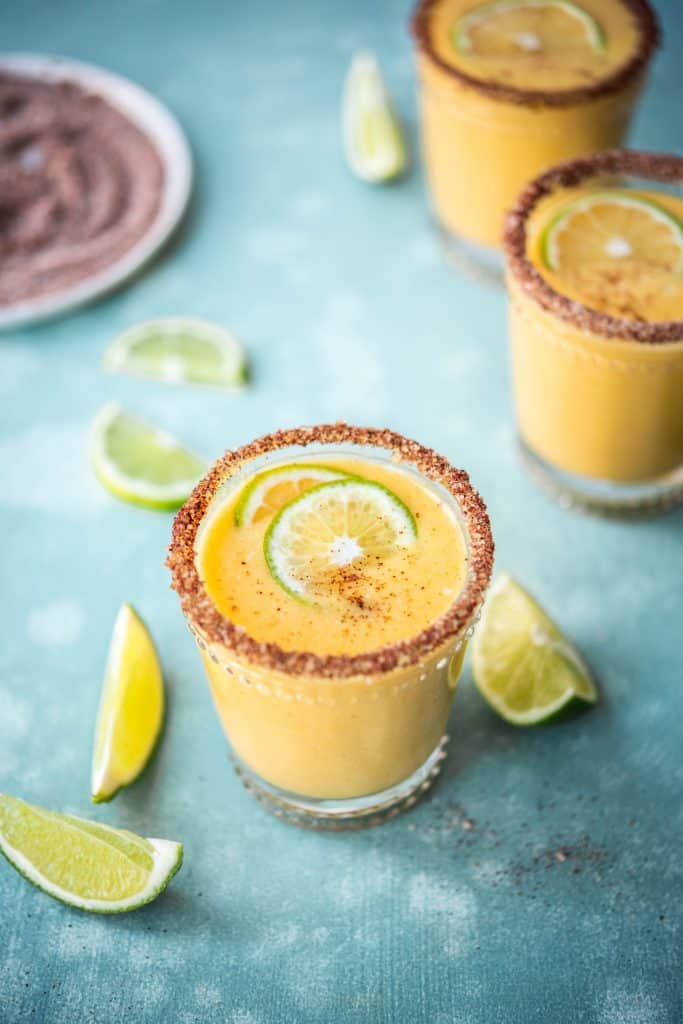 45 degree side view of mango margarita with chili salt rim on blue background
