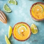 Overhead view of mango chili margaritas with limes on teal background