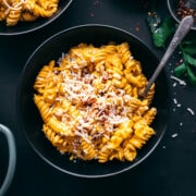 overhead view of creamy vegan roasted red pepper pasta in black bowl topped with parmesan, pine nuts and red pepper flakes.