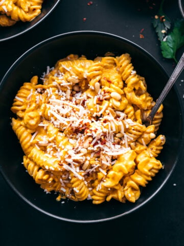 overhead view of creamy vegan roasted red pepper pasta in black bowl topped with parmesan, pine nuts and red pepper flakes.