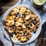 Overhead of waffles topped with sliced bananas, blueberries and maple syrup on a white plate