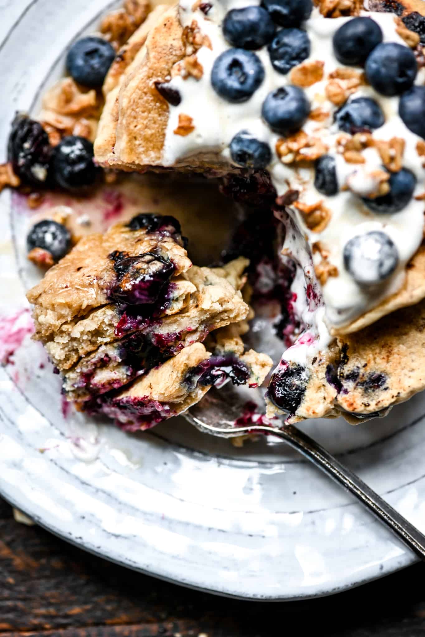 Overhead of vegan blueberry pancakes on a fork on a white plate for breakfast