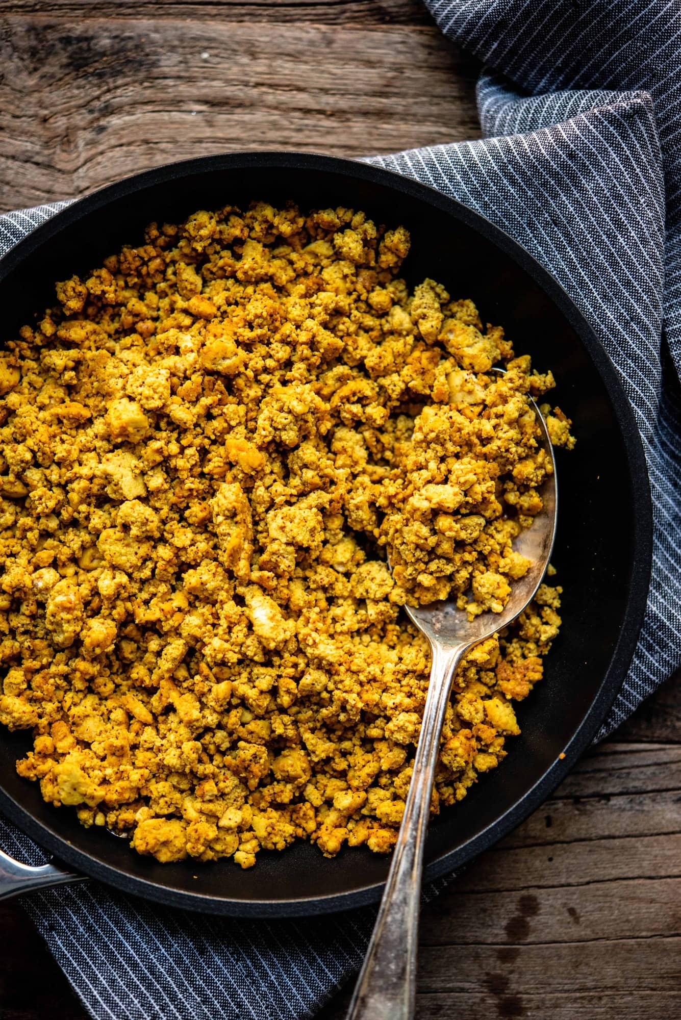 Overhead of scrambled tofu in a skillet with a spoon in it