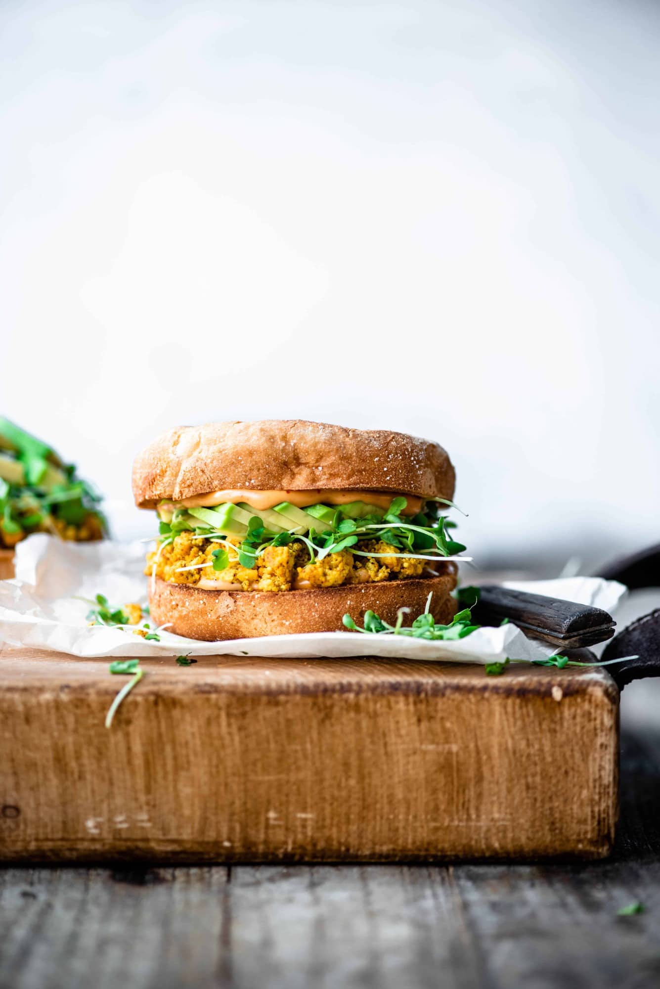 Side view of scrambled tofu and avocado breakfast sandwich on an english muffin