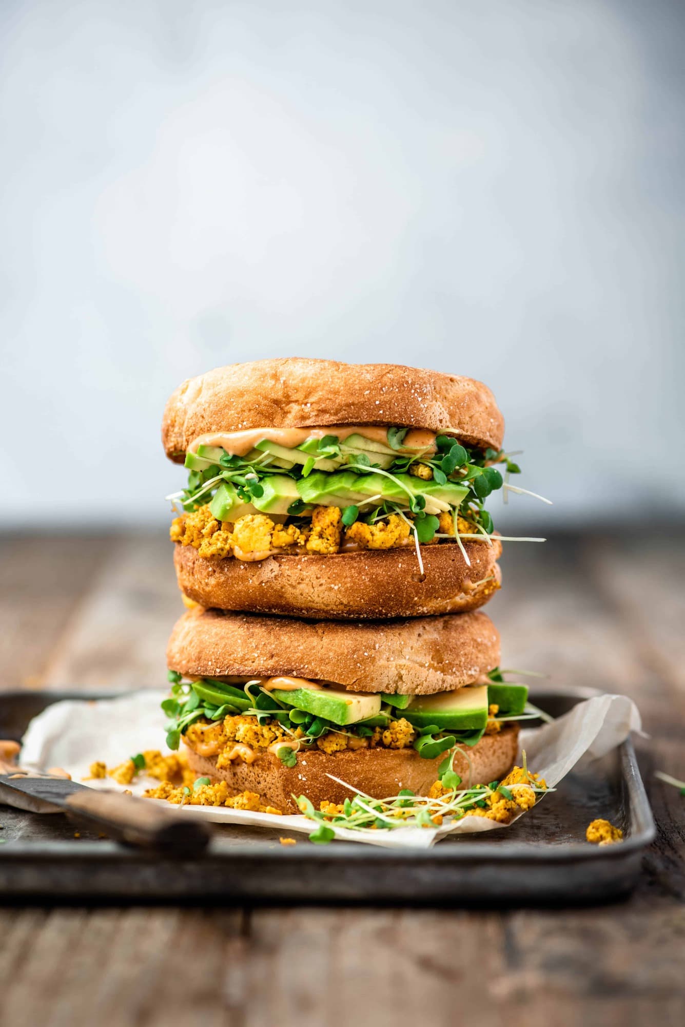 Side view of two stacked scrambled tofu and avocado breakfast sandwiches on an english muffin