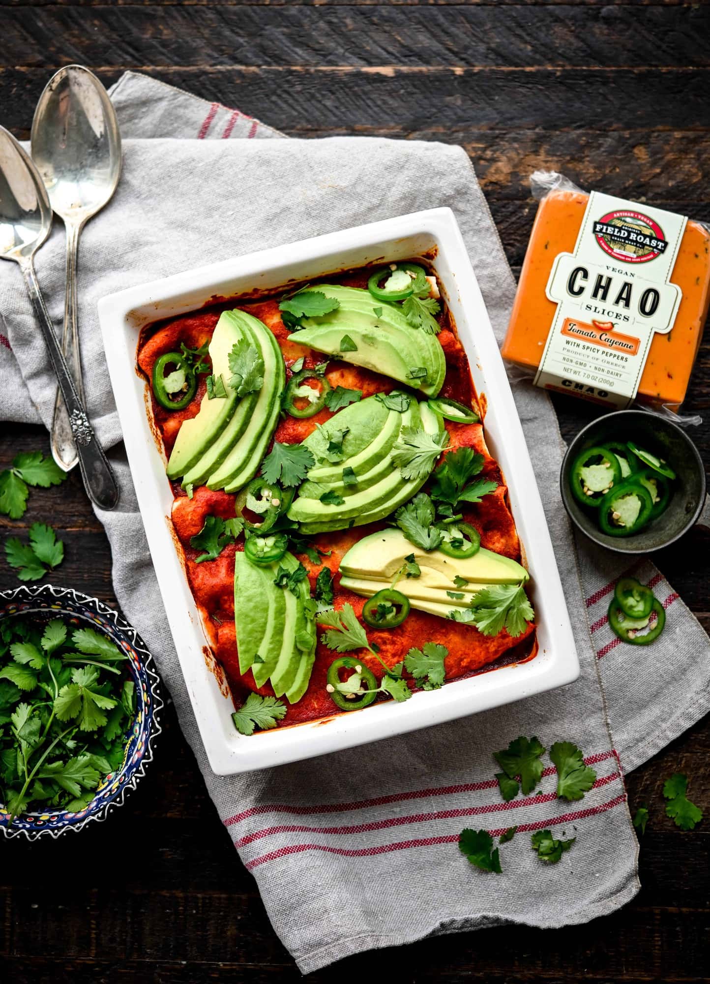 Overhead view of vegan enchiladas in white rectangular pan topped with avocado slices