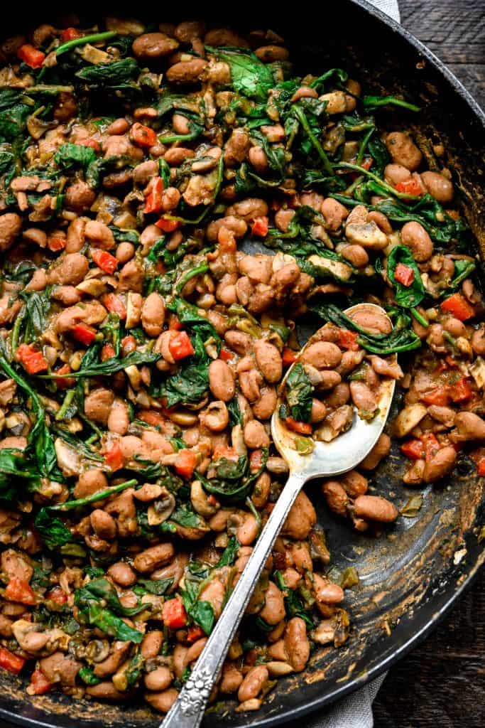 Vegan Pinto enchilada filling with mushrooms and spinach in a cast iron skillet and silver spoon