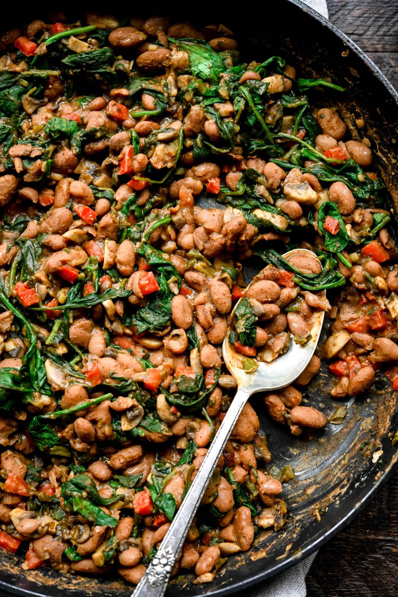 Vegan Pinto enchilada filling with mushrooms and spinach in a cast iron skillet and silver spoon