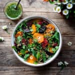 Overhead view of citrus lentil beet salad in a white bowl on a wood table with a vase of flowers