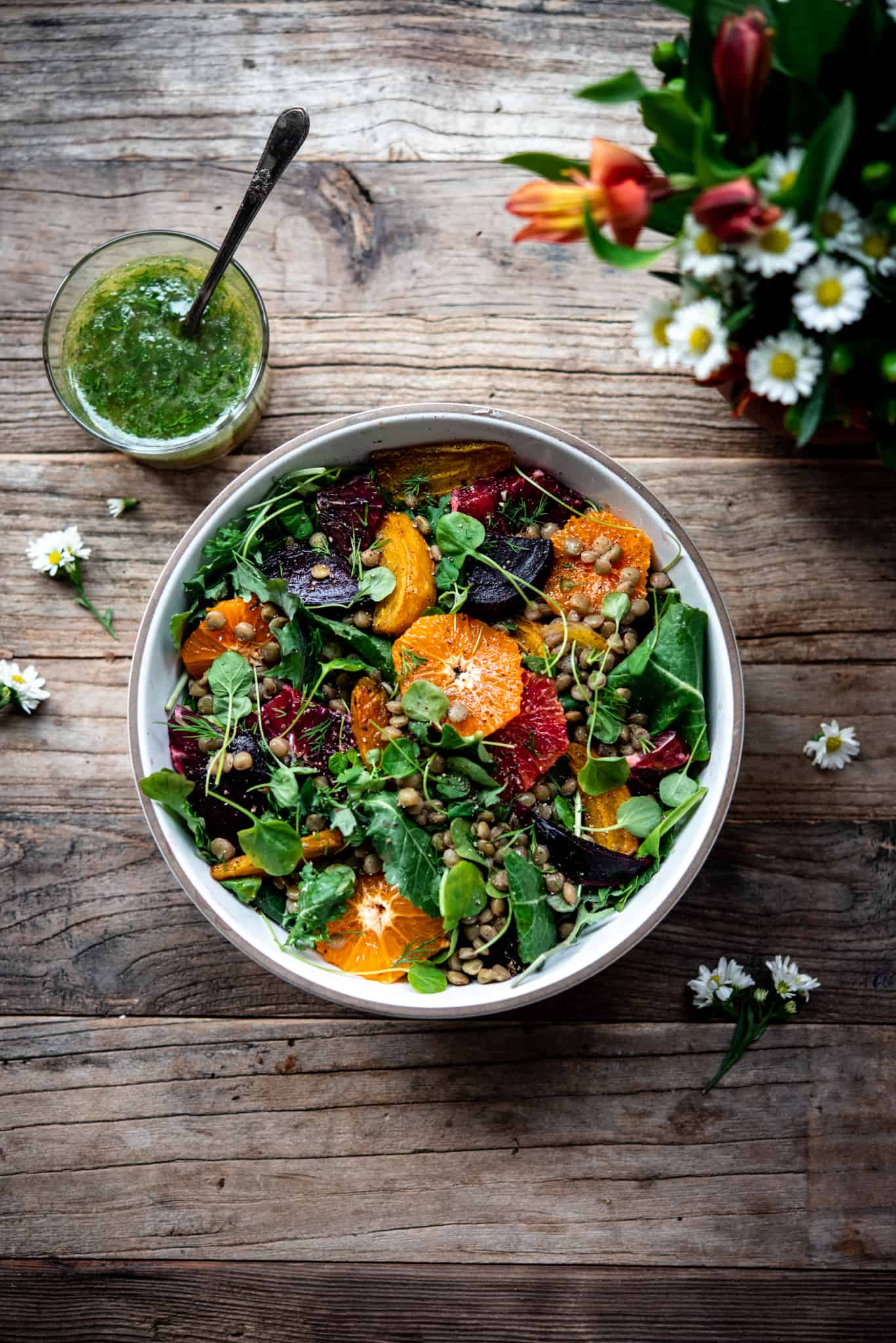 Overhead view of citrus lentil beet salad in a white bowl on a wood table with a vase of flowers