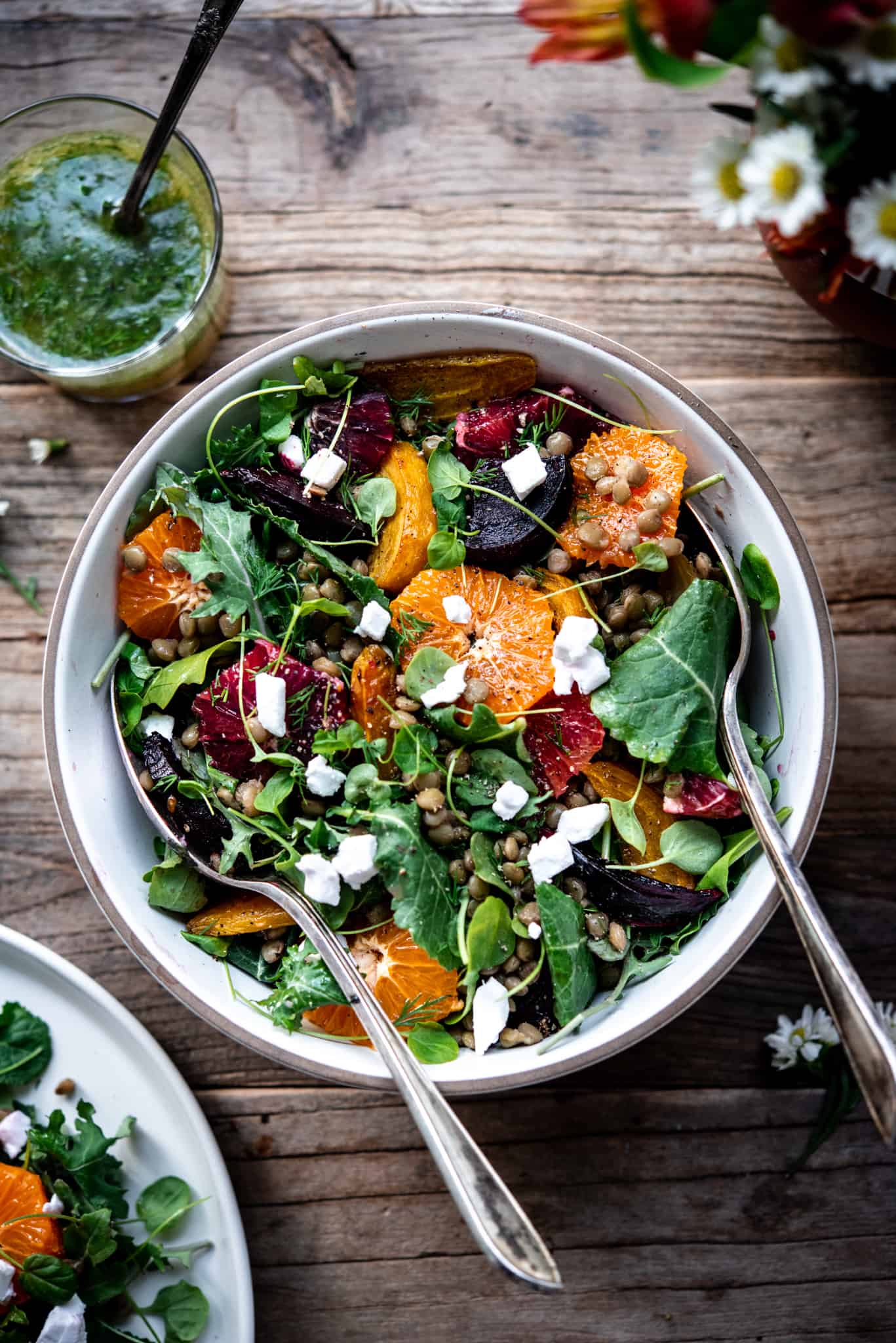 Overhead view of winter salad in a white bowl on a wood table with a vase of flowers