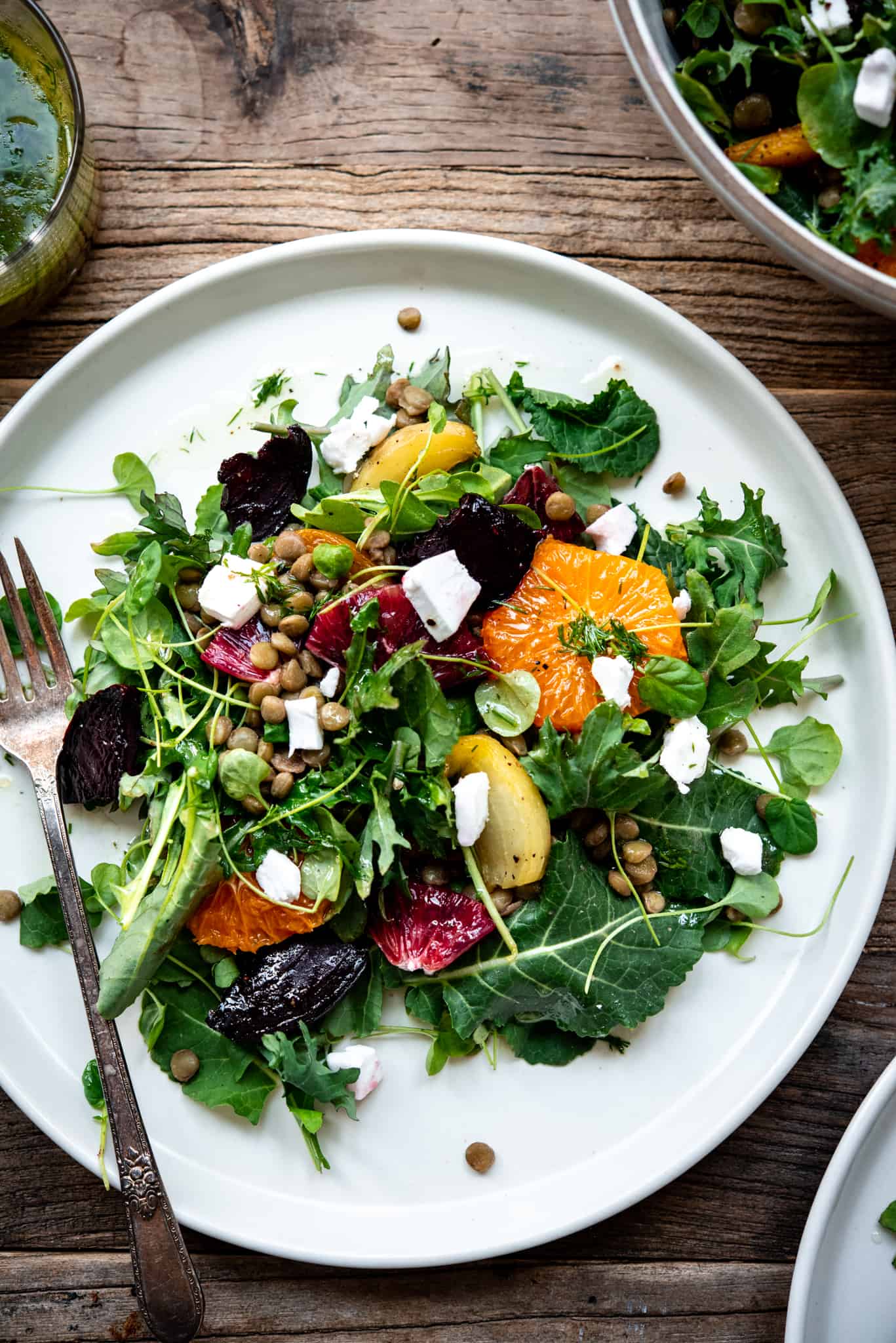 Overhead view of citrus lentil beet salad on a large white plate with a fork on a wood table