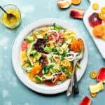 Overhead view of colorful citrus fennel avocado salad on a white plate on blue background